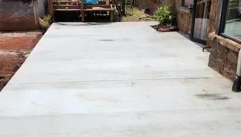 A concrete driveway leading to a house with a deck in the background.