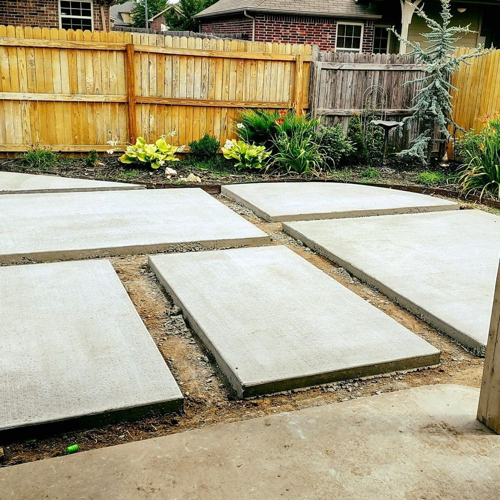A backyard with a wooden fence and concrete slabs