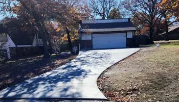 A concrete driveway leading to a garage with a house in the background.