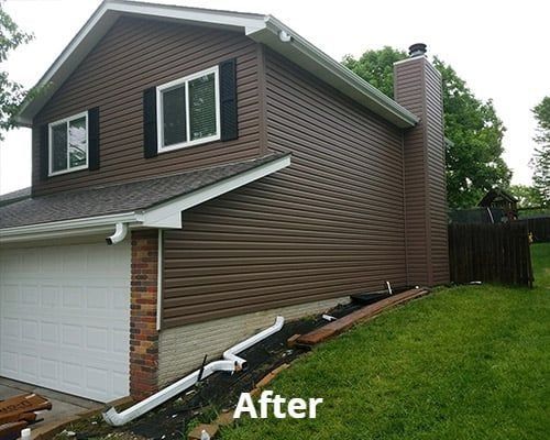 After view of brown house with white garage and sloped green lawn, showing the side of the home.