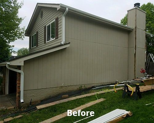 Before photo of a tan two-story house with white trim and a chimney, viewed from the side in a grassy yard