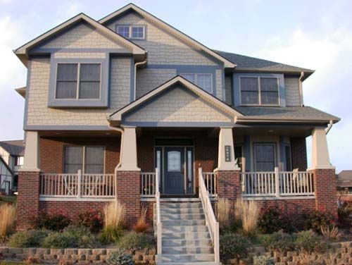 Front view of a two-story gray house with a covered porch, white columns, and brick steps