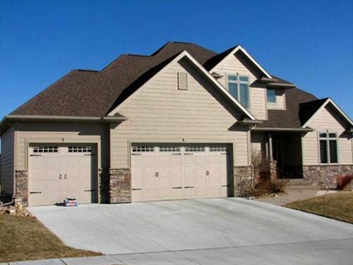 Suburban house with three-car garage, beige siding, stone accents, and a sloped driveway
