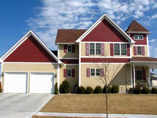 Suburban house with red and beige siding, two-car garage, and front porch under a blue sky