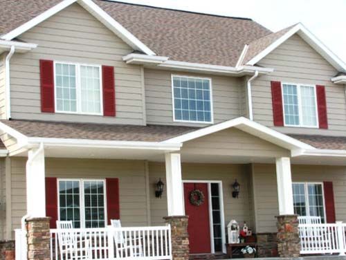 Two-story beige house with red shutters, white porch railings, and a red front door