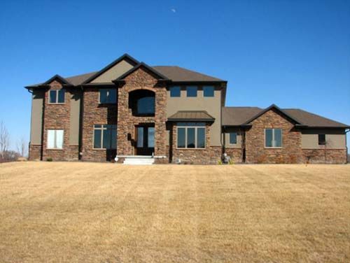 Large brick suburban house with a two-story front, arched entry, and a wide dry lawn under a clear blue sky
