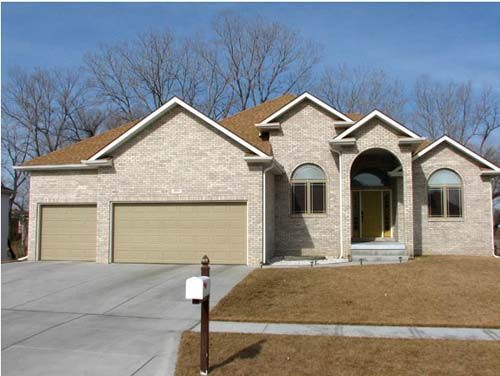 Suburban brick house with two garages, arched windows, and a front lawn under a clear blue sky