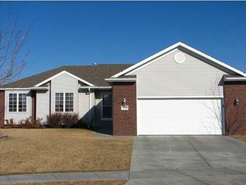 Single-story suburban house with brick facade, white garage door, and driveway under a clear blue sky