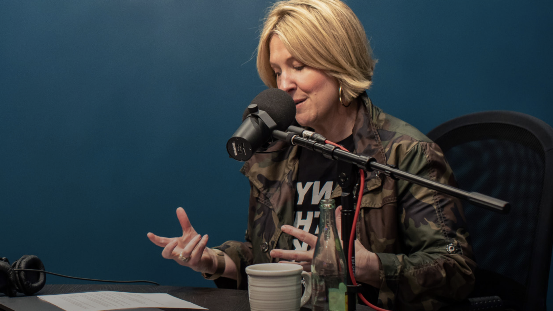 A woman is sitting at a table talking into a microphone.