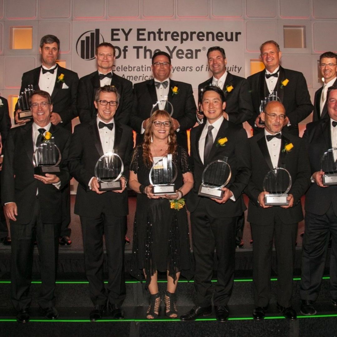 A group of people holding trophies in front of a sign that says ey entrepreneur of the year