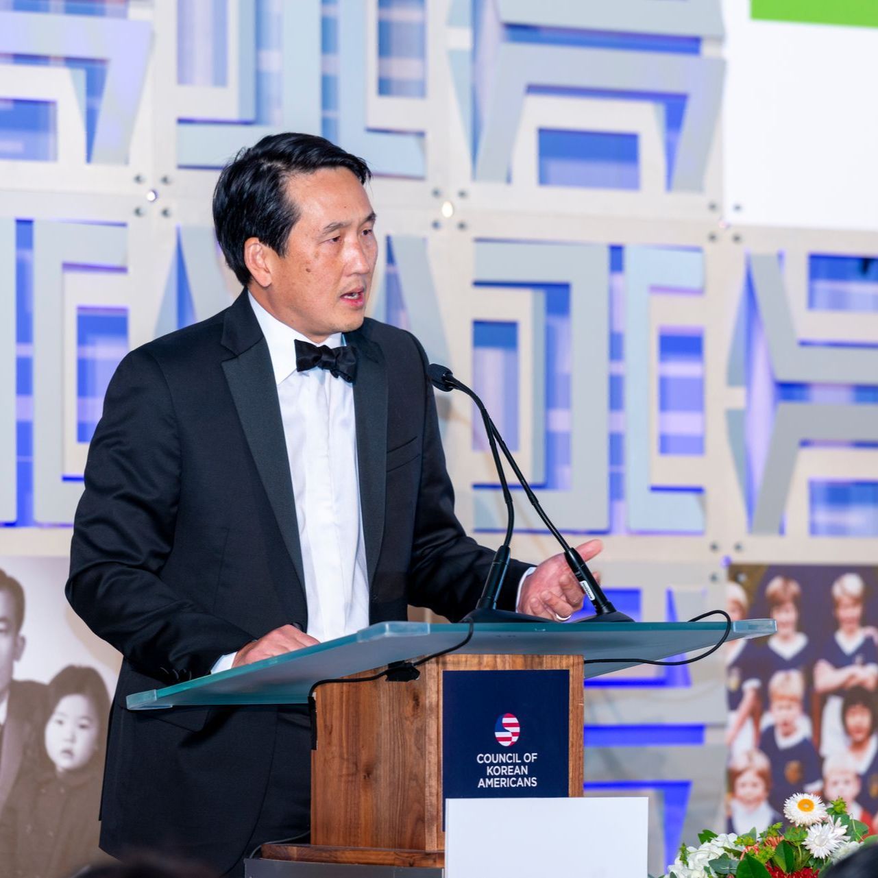 A man in a tuxedo is standing at a podium giving a speech
