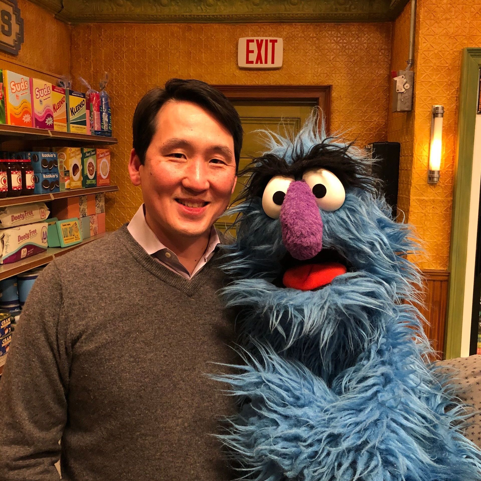 A man standing next to a stuffed animal in front of an exit sign