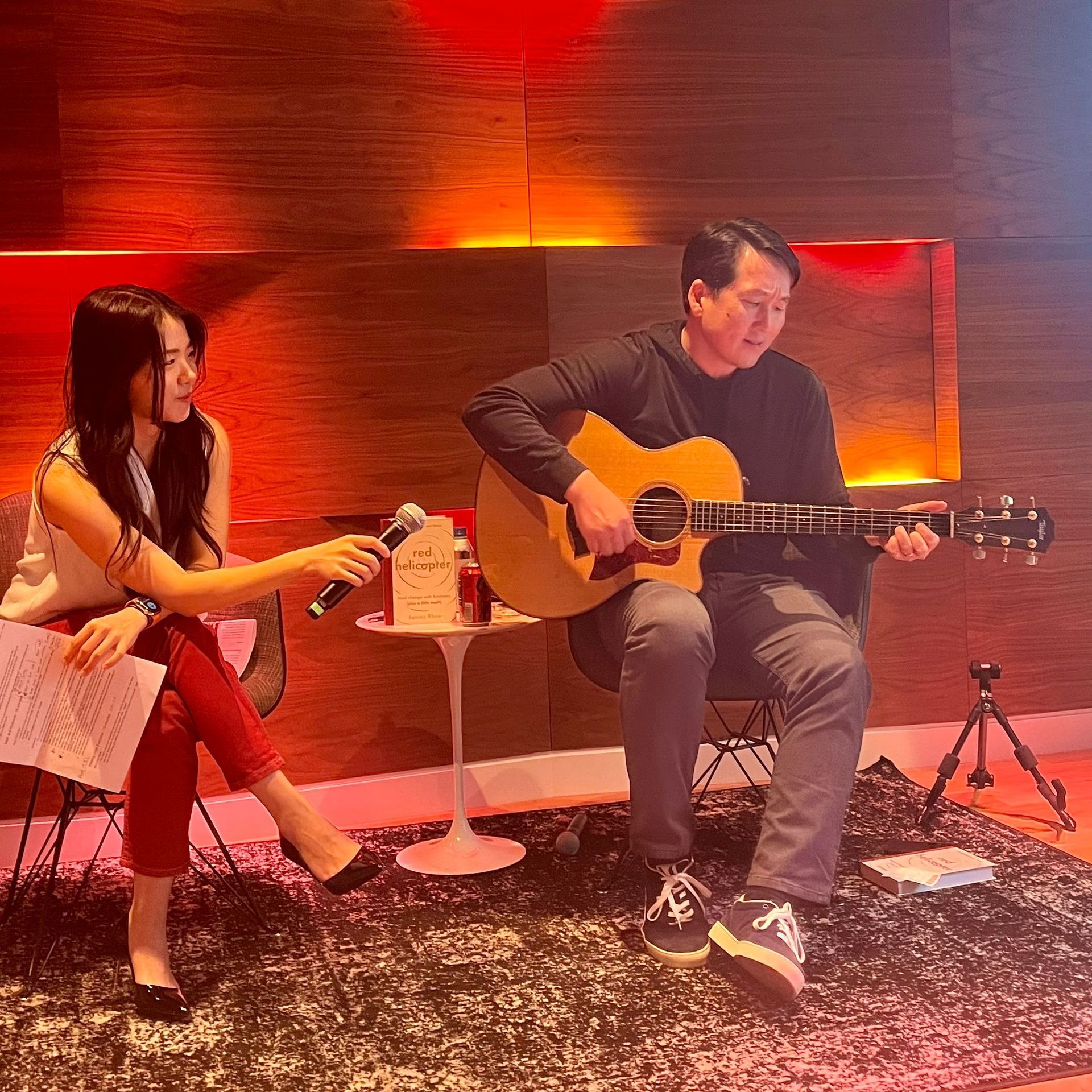 A man is playing a guitar and a woman is sitting next to him holding a microphone.