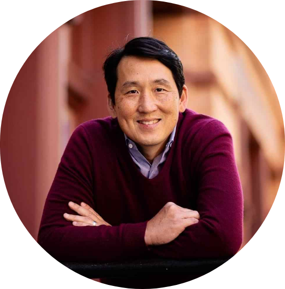 A man in a purple sweater is smiling with his arms crossed