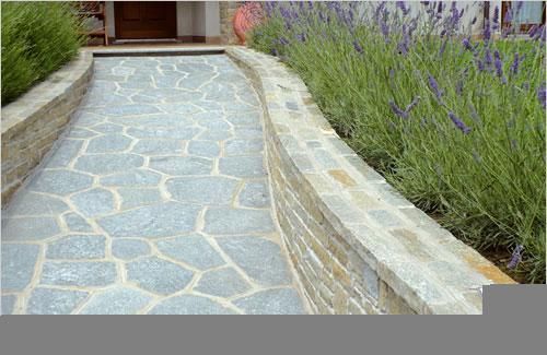 Un sentiero in pietra che conduce a una casa con fiori viola sullo sfondo.