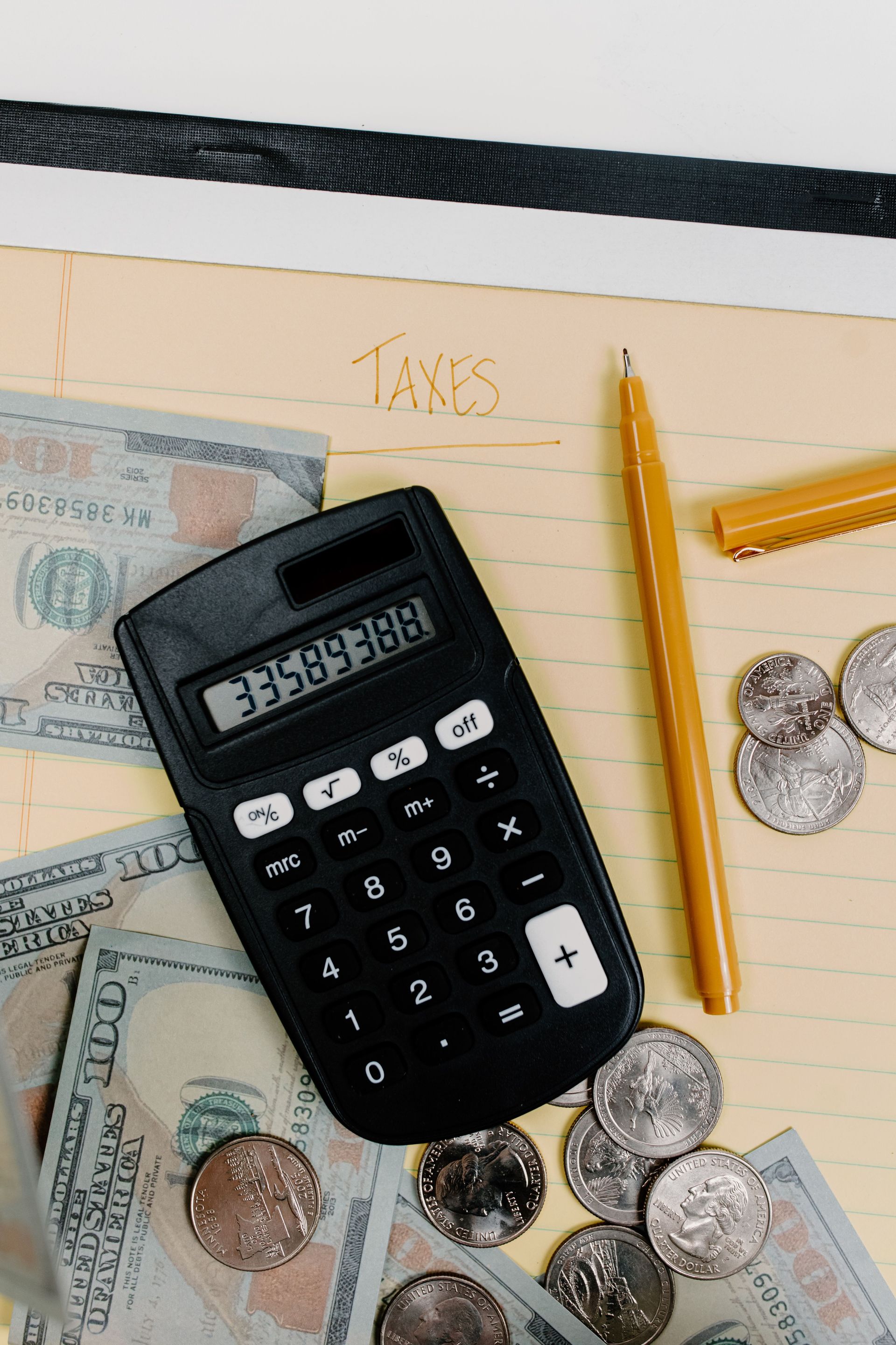 Calculator, pencils, and coins on a desk with paper currency and a notebook.