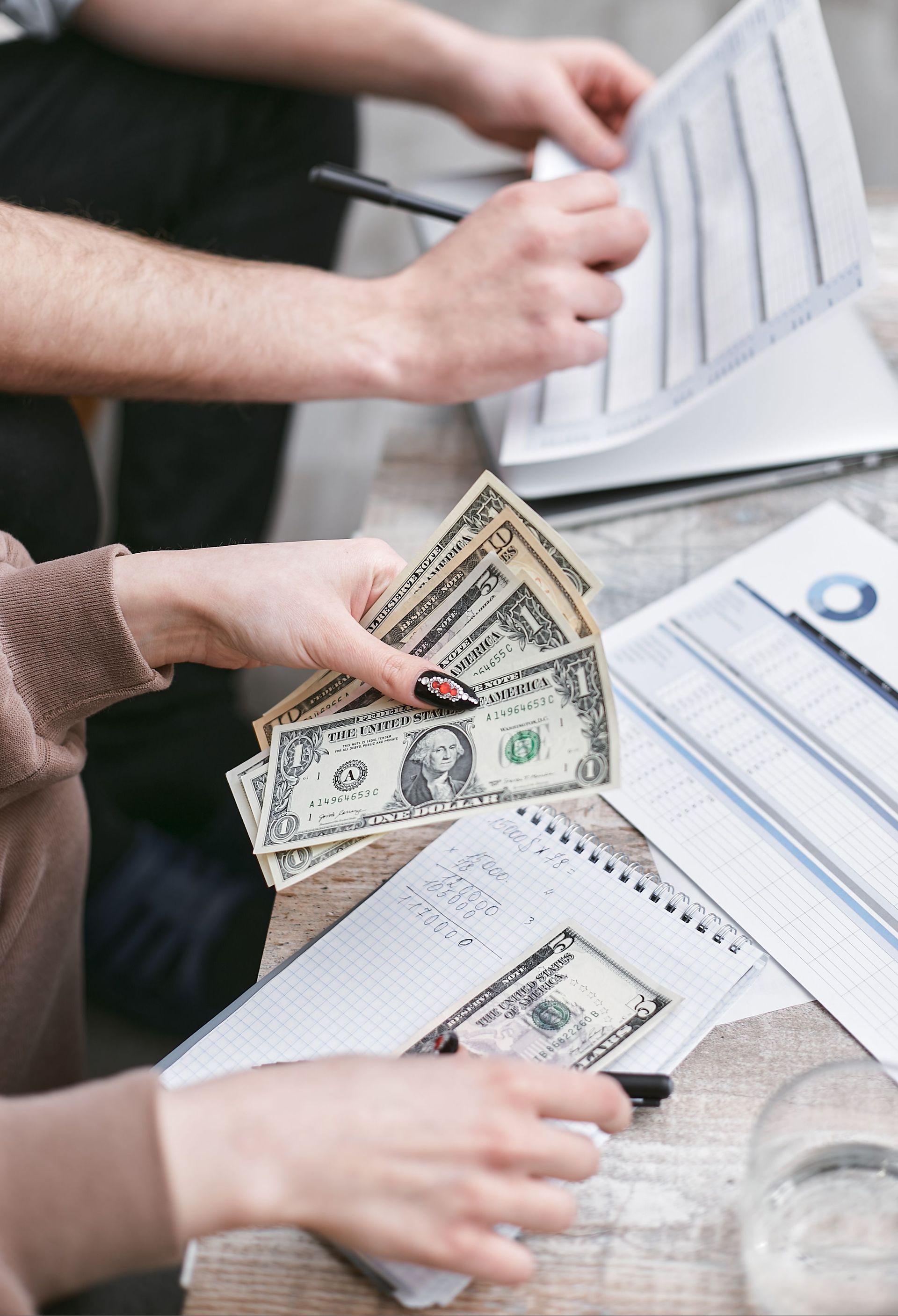 Hands exchanging cash beside documents and a laptop during a financial transaction
