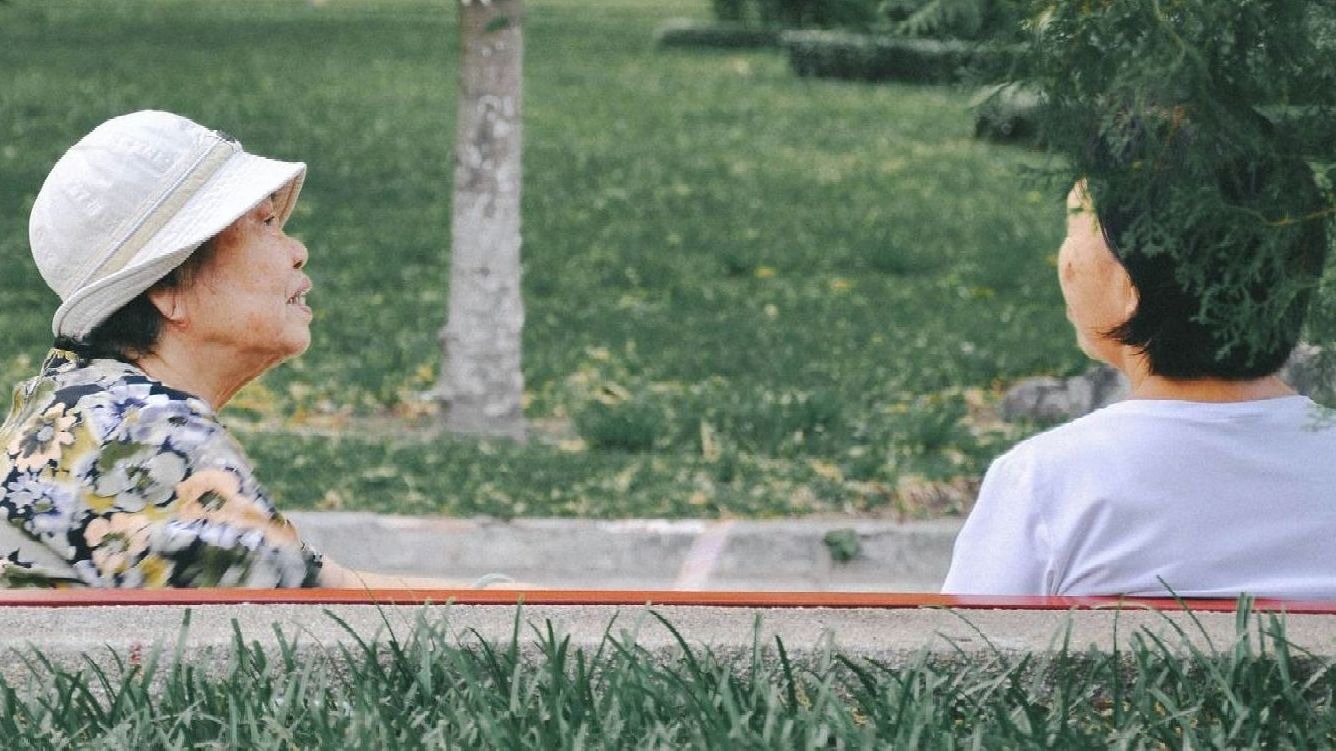Two women sitting on a bench chatting.