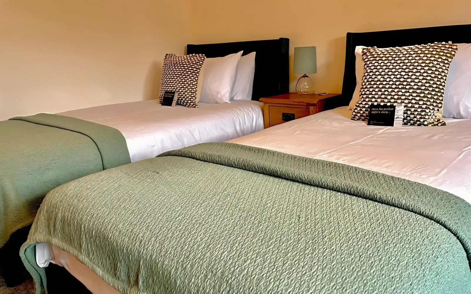 Two neatly made twin beds with green blankets and patterned pillows in a hotel room