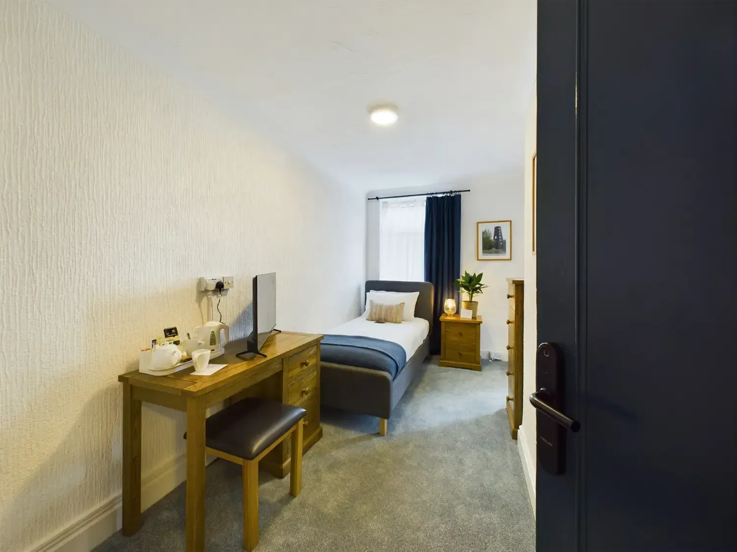 Compact bedroom with desk, bed, window, and dark door in a simple modern interior
