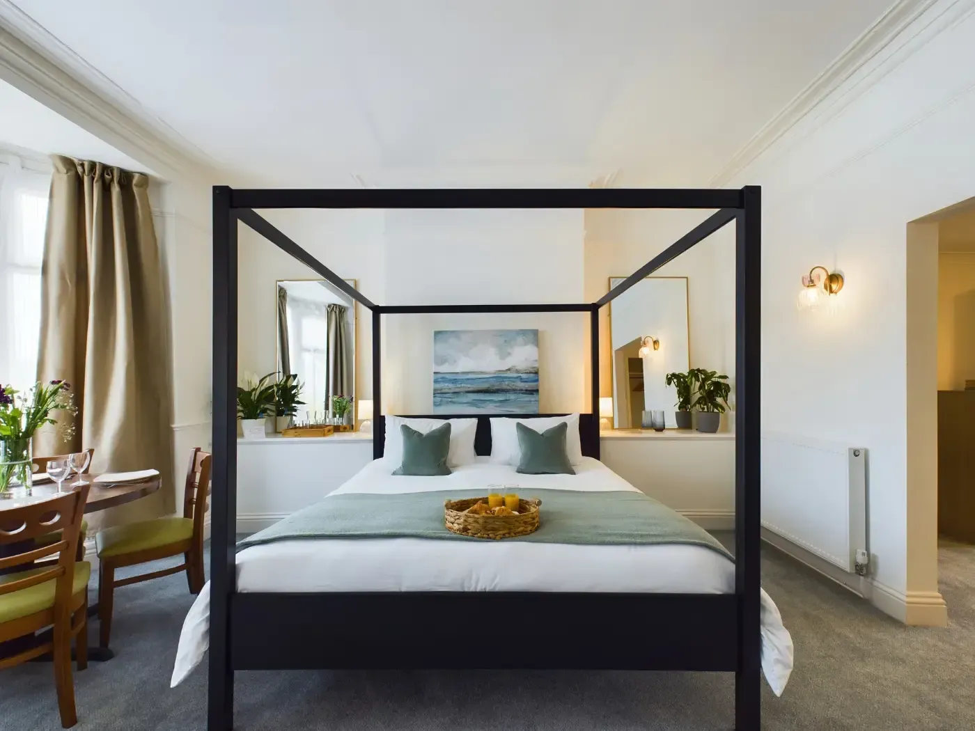 Modern bedroom with a black canopy bed, white walls, and windows letting in natural light