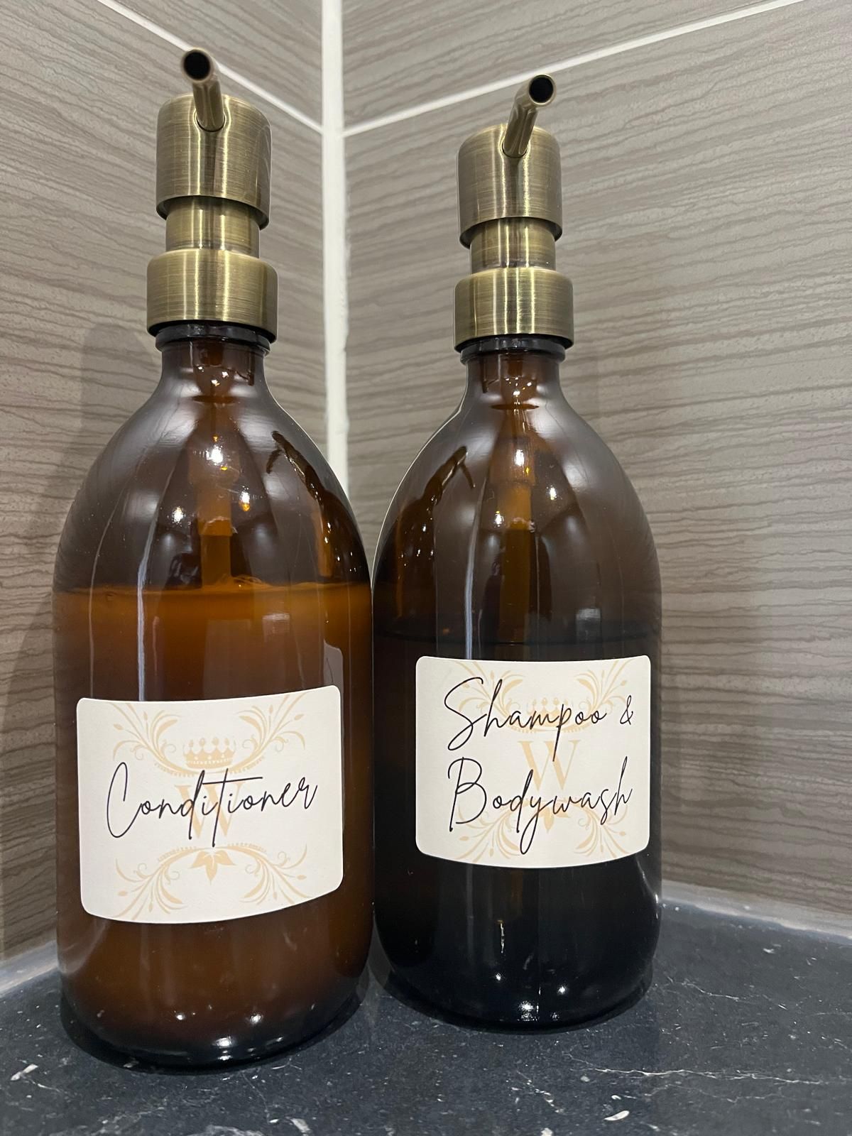 Two amber glass bottles with gold pump tops and handwritten white labels on a wooden surface.