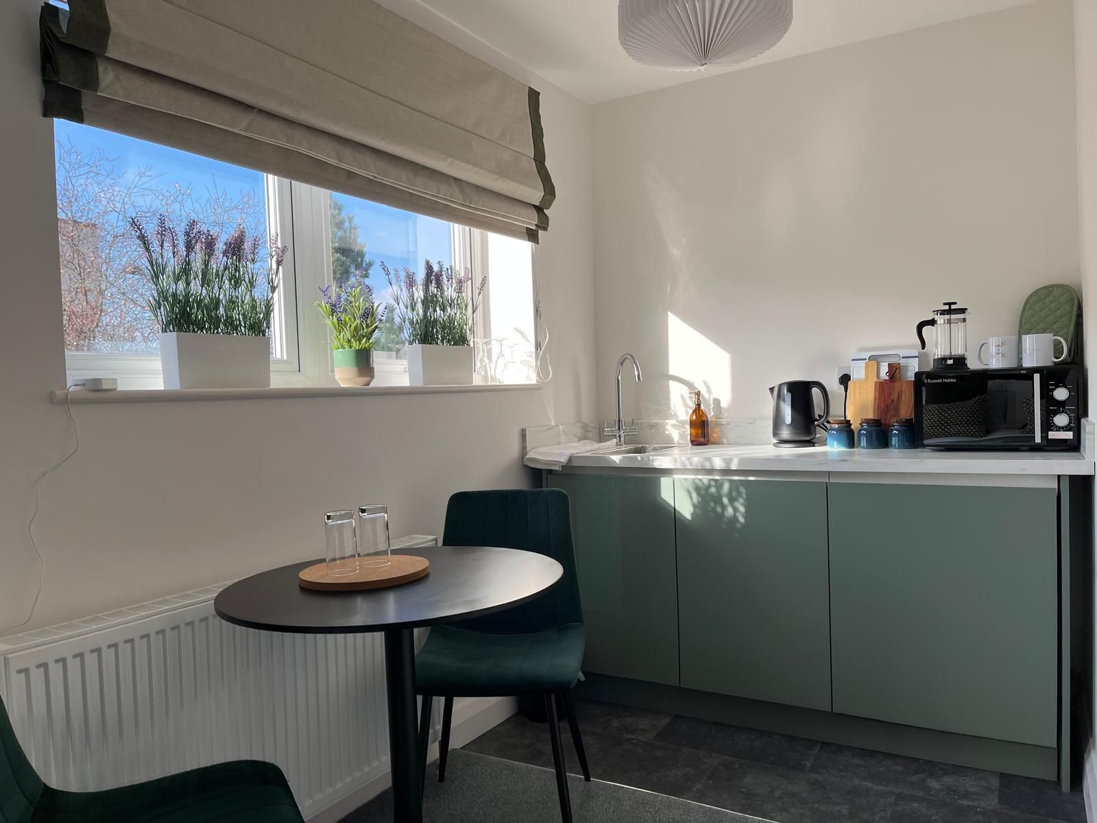 Small kitchen nook with black table and chair, green cabinets, and sunlight streaming through a window.