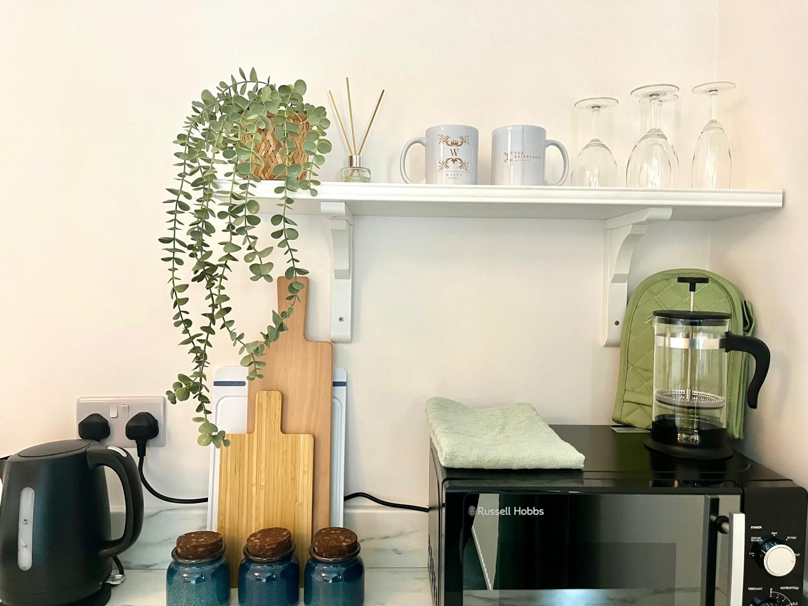 Kitchen counter with coffee maker, toaster oven, kettle, mugs, glasses, and a trailing plant on a shelf