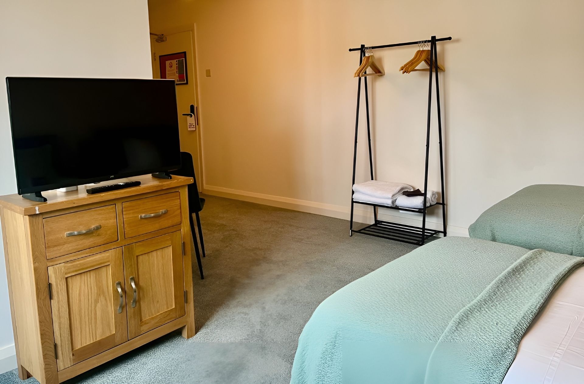 Bedroom with two beds, a TV on a wooden cabinet, and a standing clothes rack