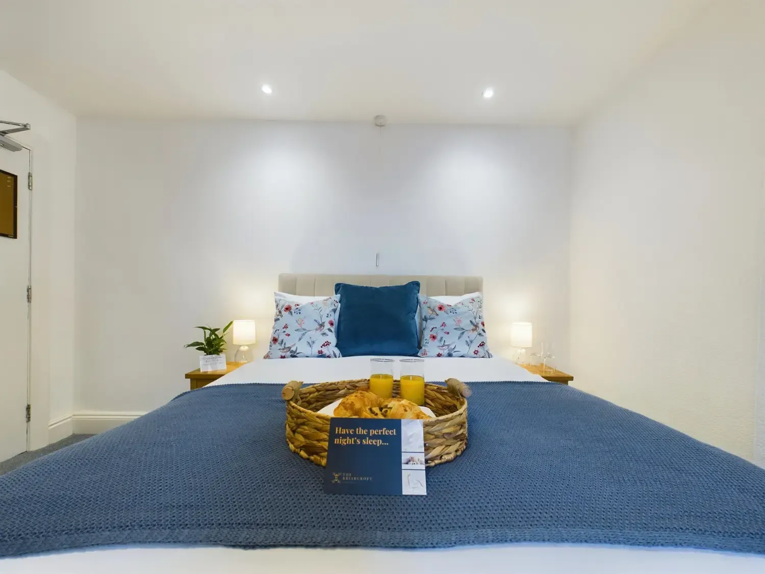Modern bedroom with a blue bedspread, decorative pillows, and a tray of fruit at the foot of the bed
