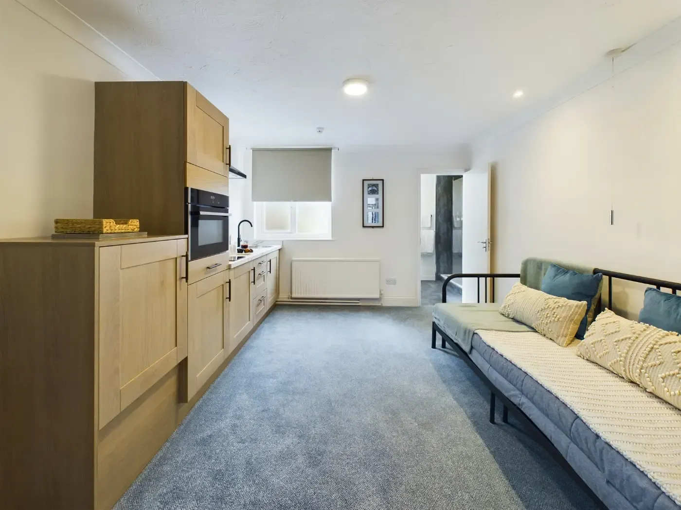Modern studio apartment with kitchenette, sofa bed, and window, in light wood and gray tones