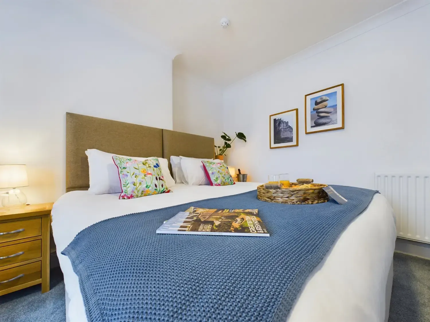 Bright bedroom with a bed, blue blanket, colorful pillows, and framed wall art