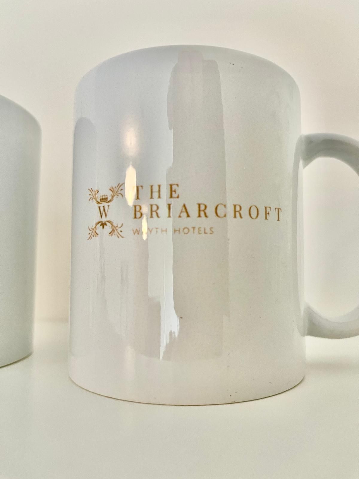 White ceramic mug with gold “The Briarcroft Hotel” logo and handle on the right
