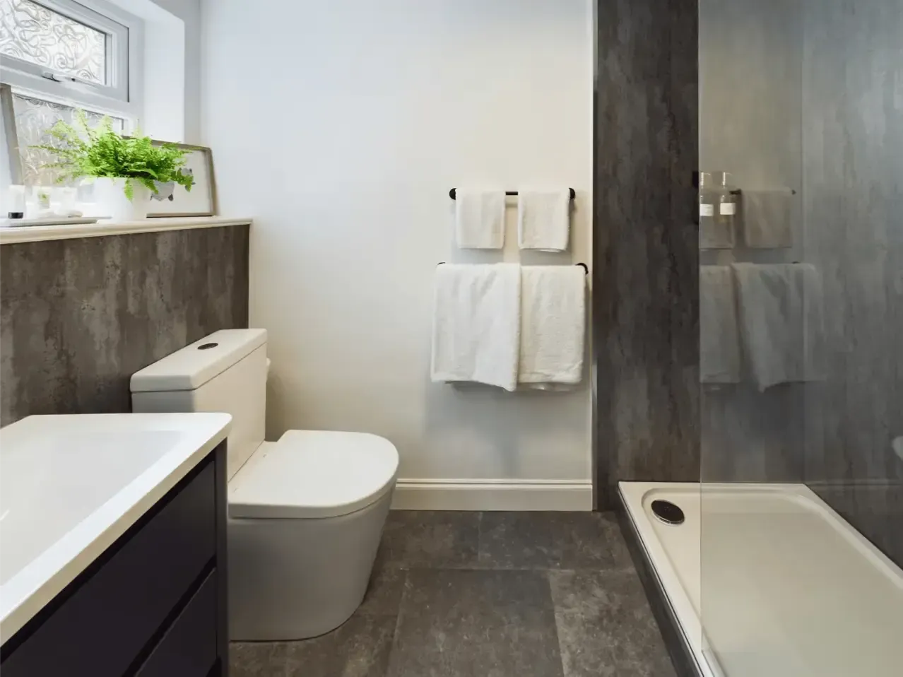 Modern bathroom with gray tile, white vanity and toilet, towel rack, and bathtub with shower panel