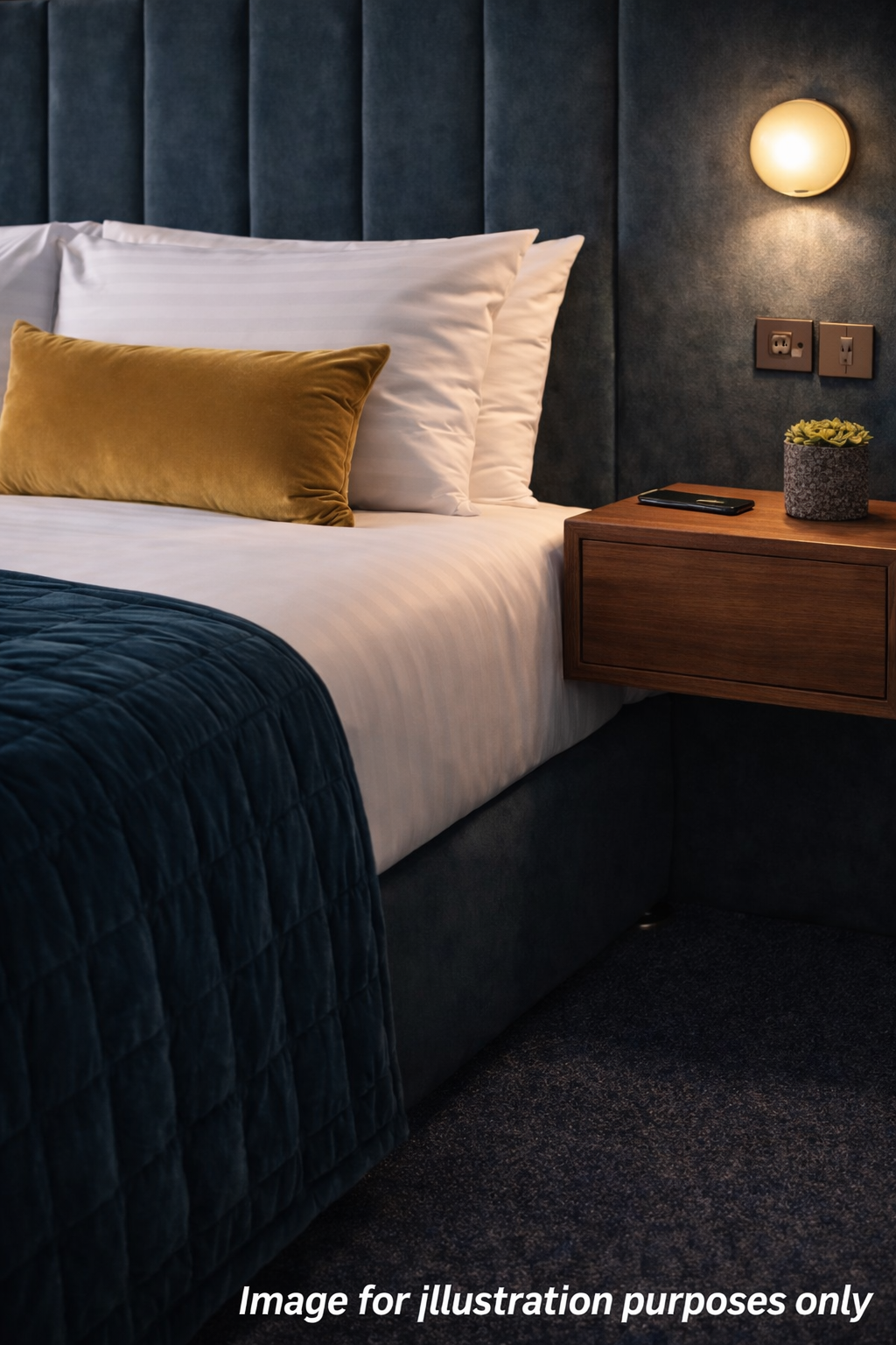 Modern bedroom with a white bed, mustard pillow, dark blanket, and wooden bedside table with lamp.