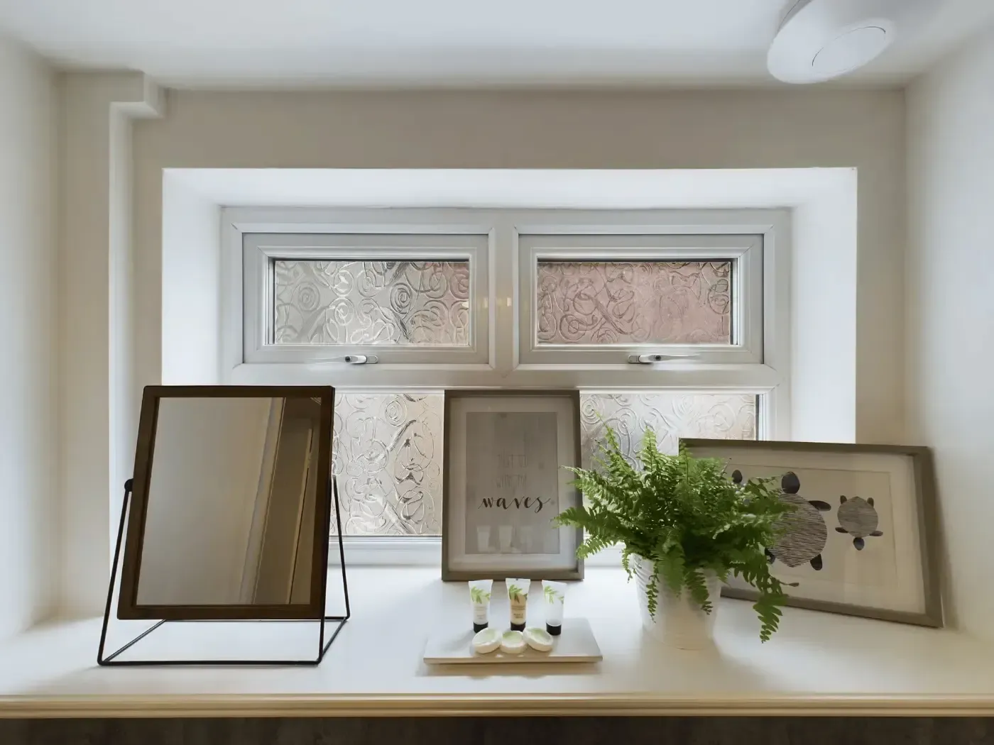 Framed wall art and a potted plant arranged on a white windowsill in a bright room