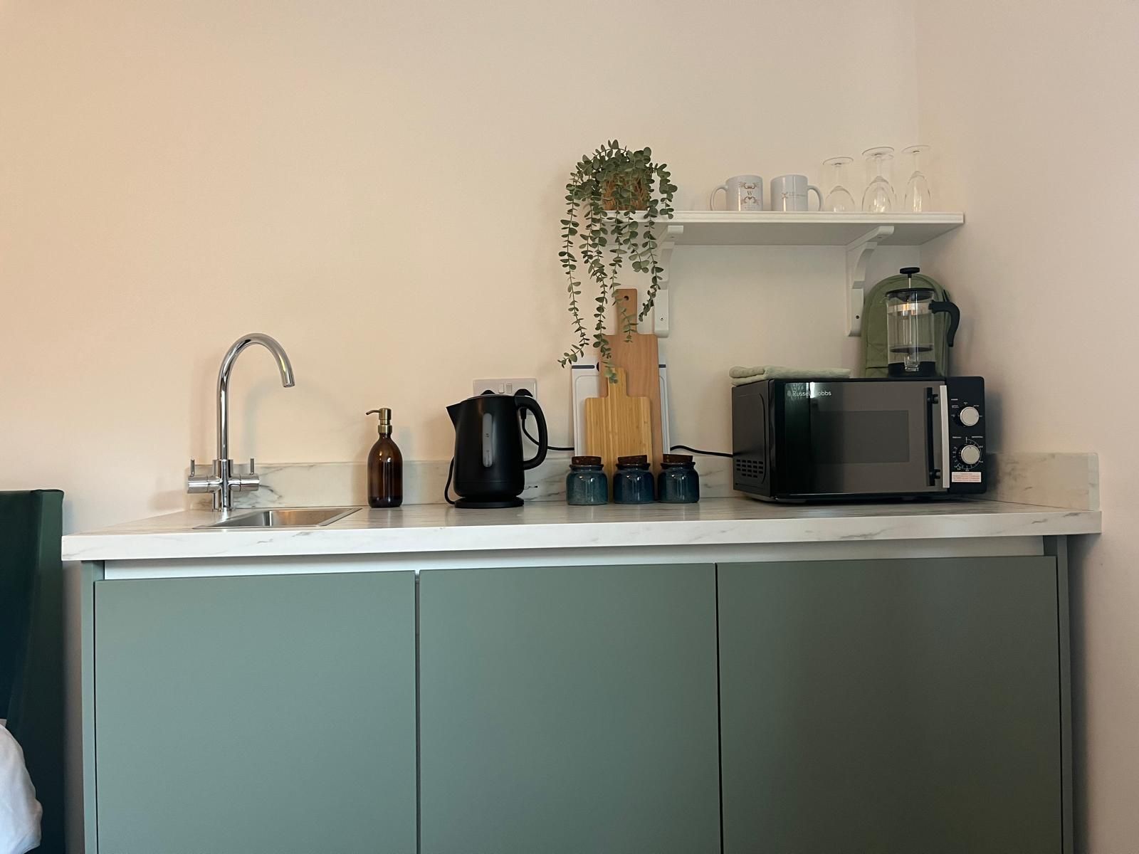 Modern kitchen counter with sink, kettle, coffee maker, toaster, and plant on a white shelf
