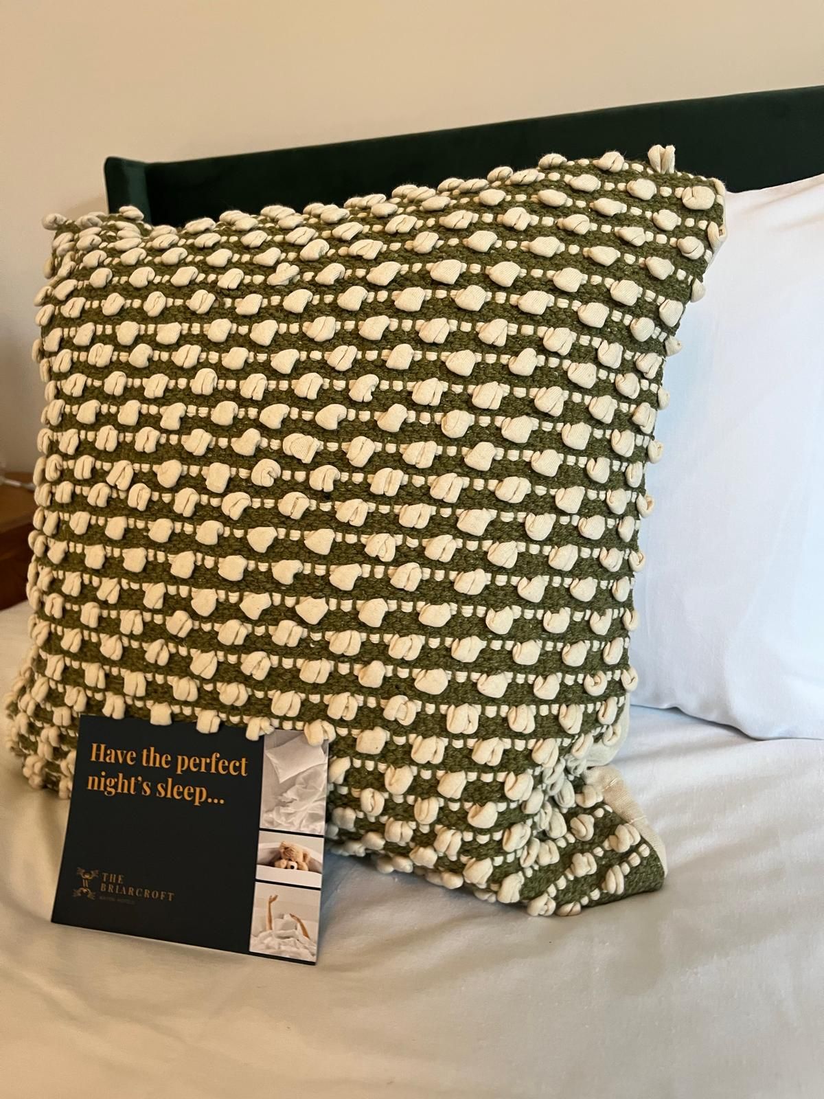 Black-and-white patterned pillow on a bed with a white pillow and small book in front