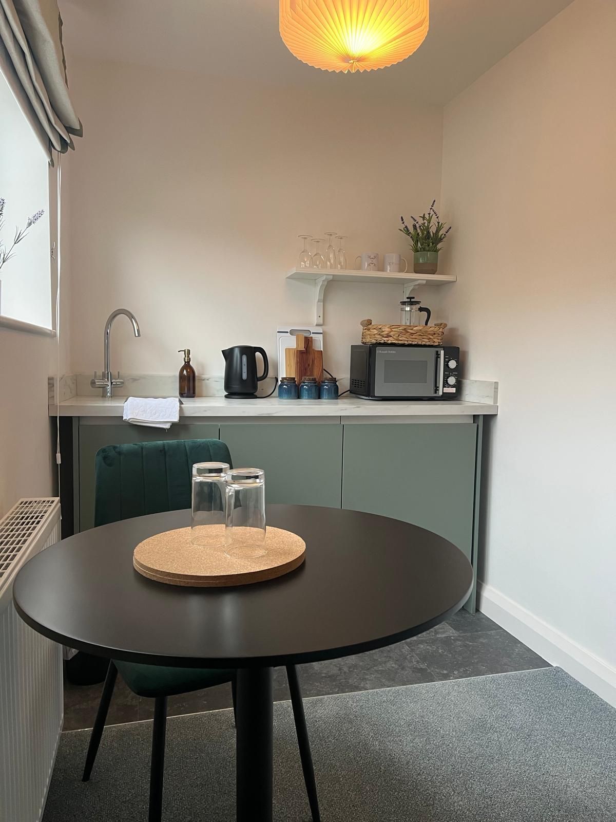 Small kitchen with black table, green cabinets, sink, microwave, and a warm ceiling light.