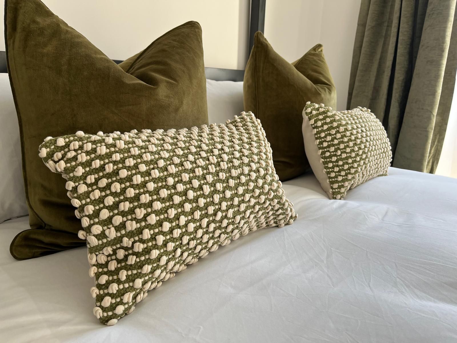 Bed with white bedding and olive and patterned throw pillows in a cozy bedroom with curtains