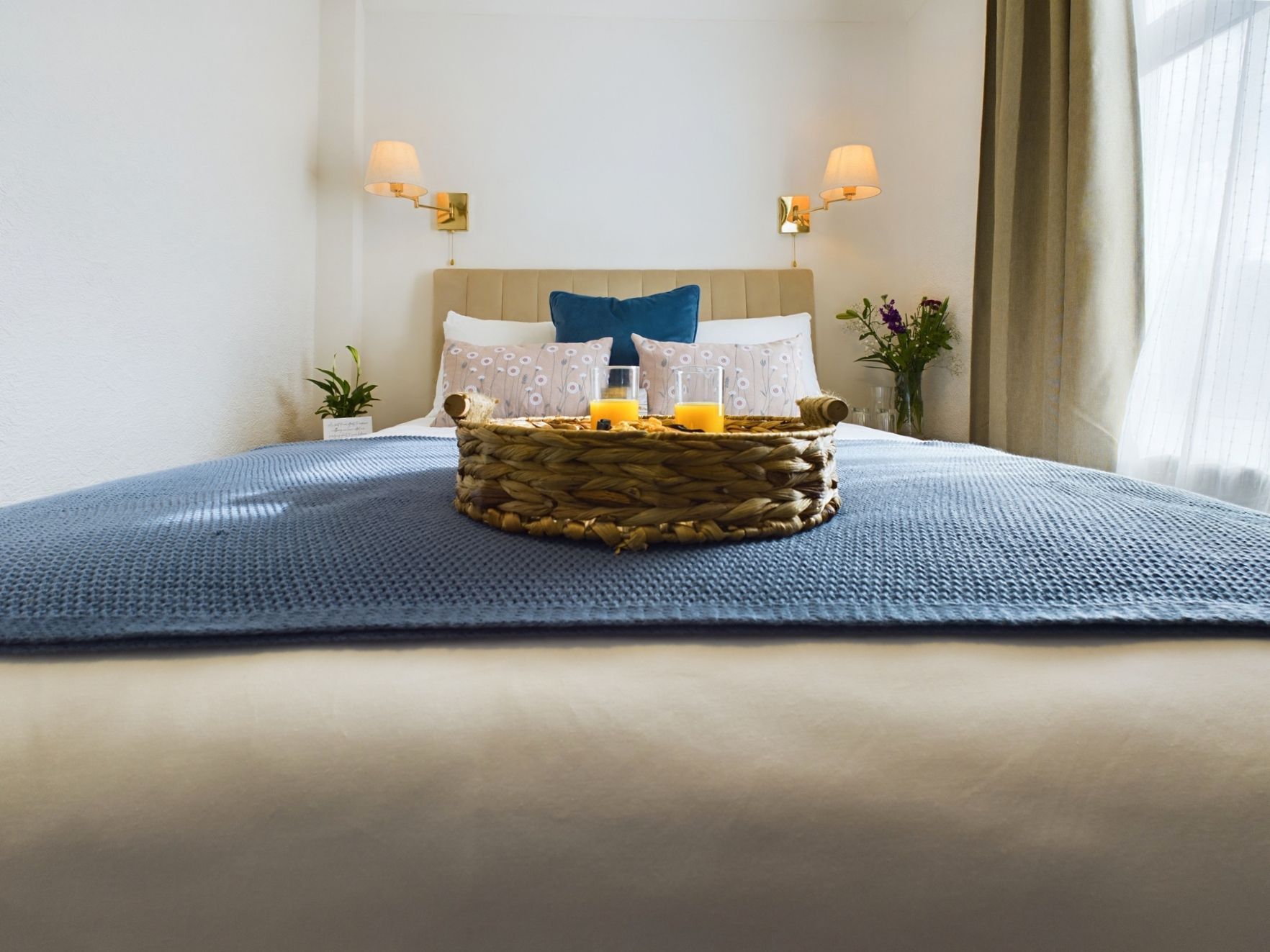 Bright bedroom with a made bed, blue blanket, and breakfast tray on the duvet