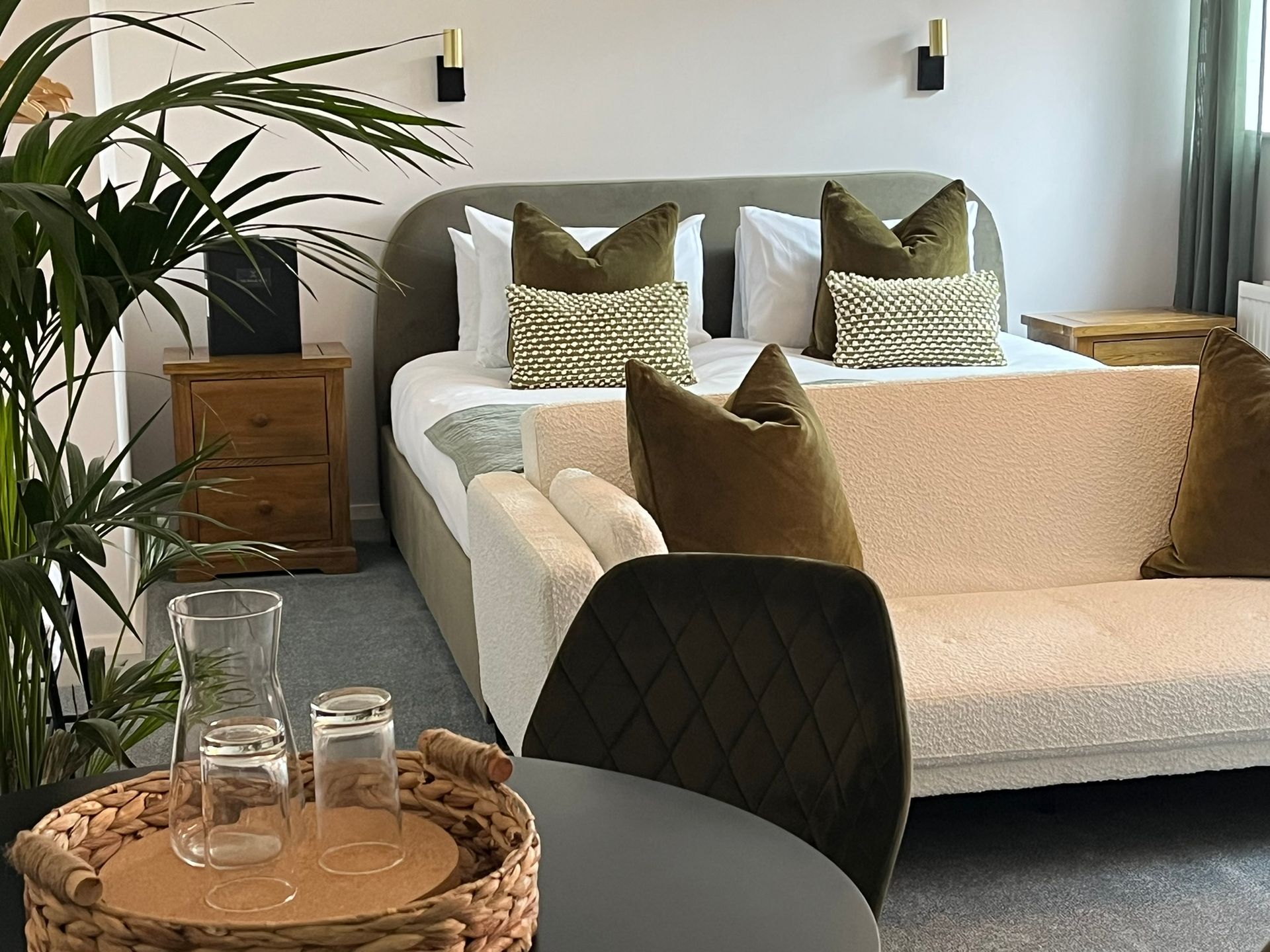 Modern living room with white sectional sofa, patterned cushions, side tables, plants, and a tray with glasses on a table