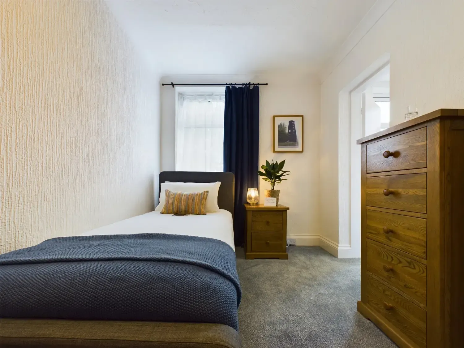 Small bedroom with a bed, nightstand, window, and wooden dresser in soft neutral tones