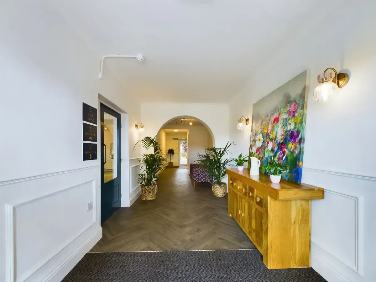 Bright hallway with white walls, wood floor, potted plants, and colorful floral artwork on the right wall
