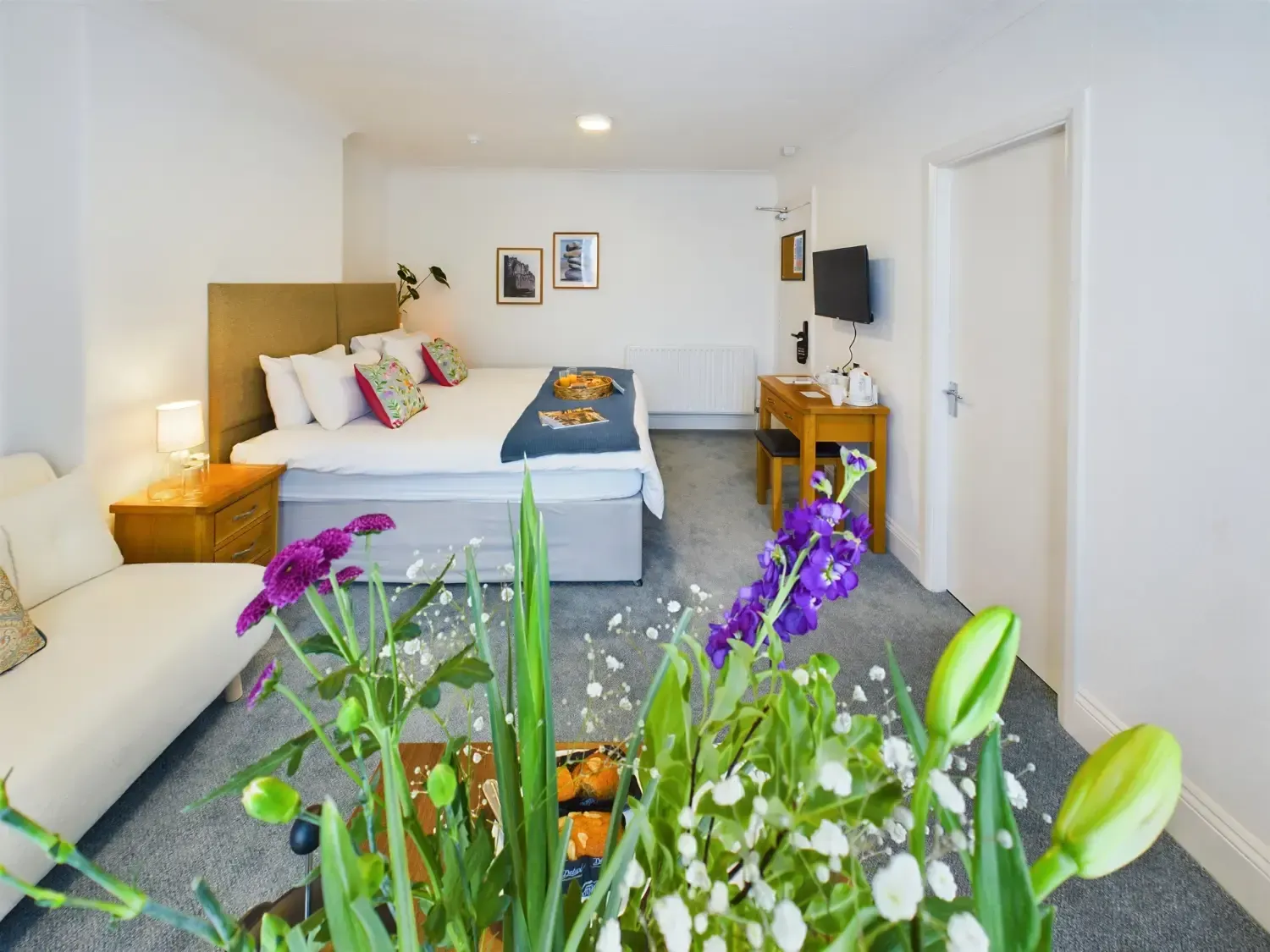Bright bedroom with a bed, sofa, desk, and a bouquet of flowers in the foreground