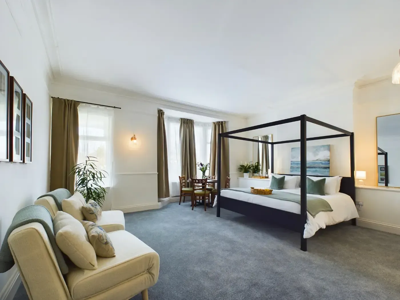Bright bedroom with a black four-poster bed, gray carpet, white sofa, and large windows.