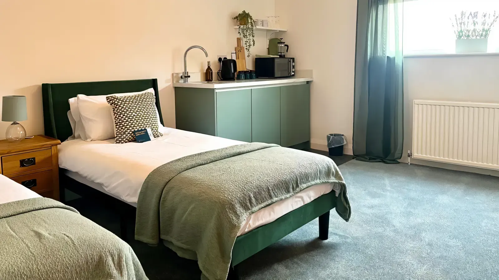 Bright bedroom with a single bed, bedside table, dresser, and window with curtains.