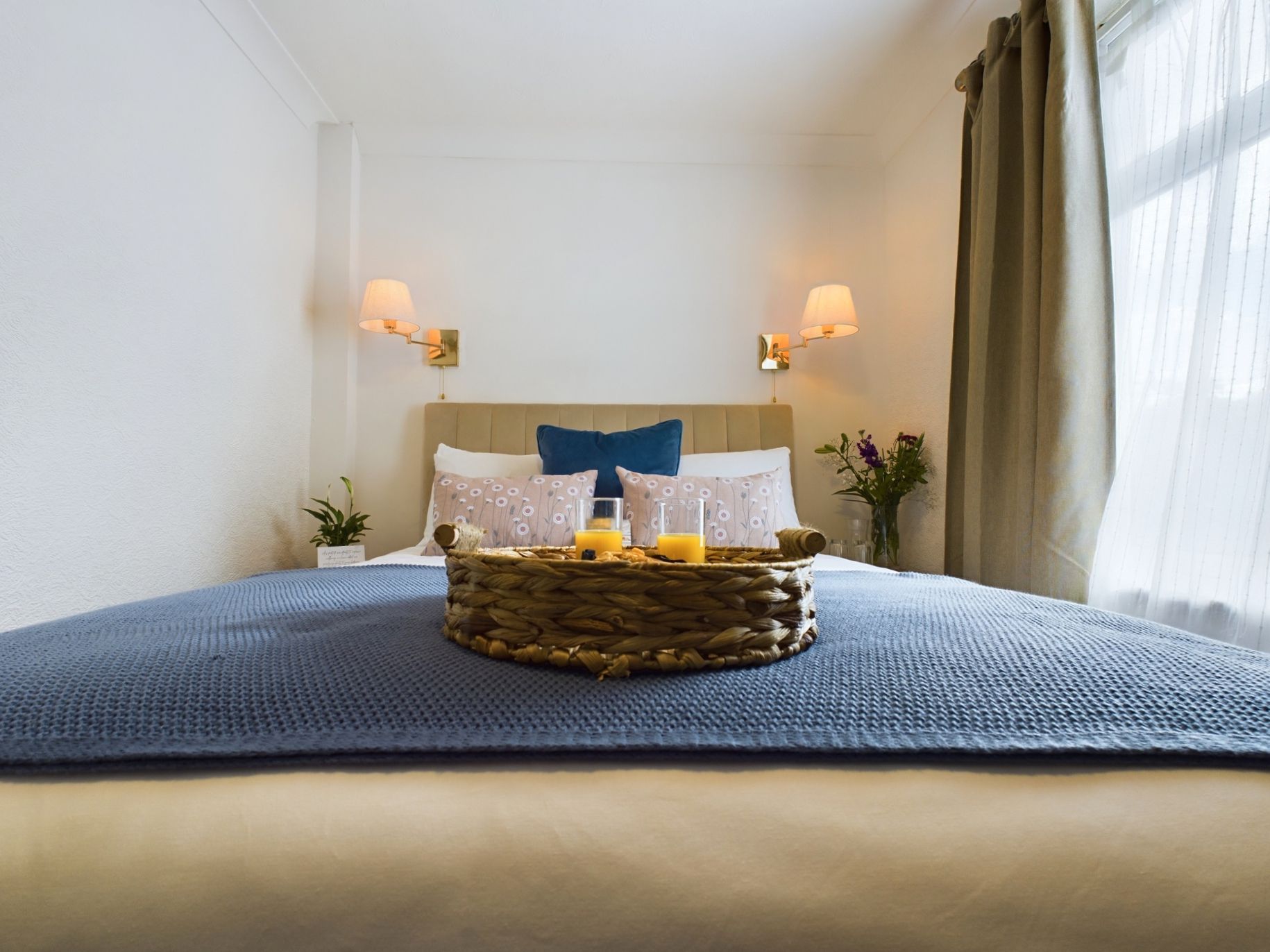 Cozy bedroom with a bed, wicker tray, bedside lamps, and blue bedding in a bright white room