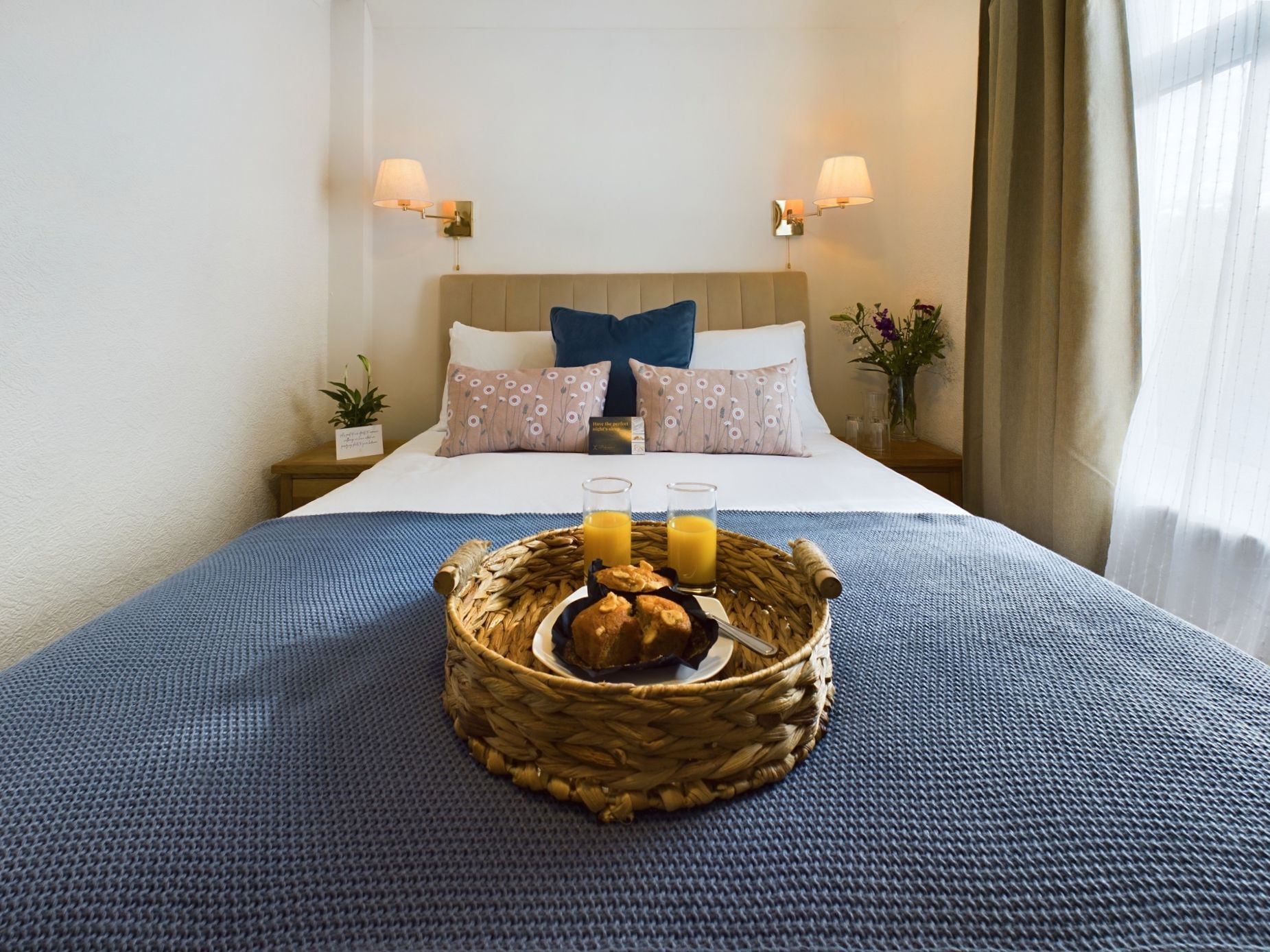 Cozy bedroom with a blue bedspread, wicker tray, candles, and flowers beside the bed