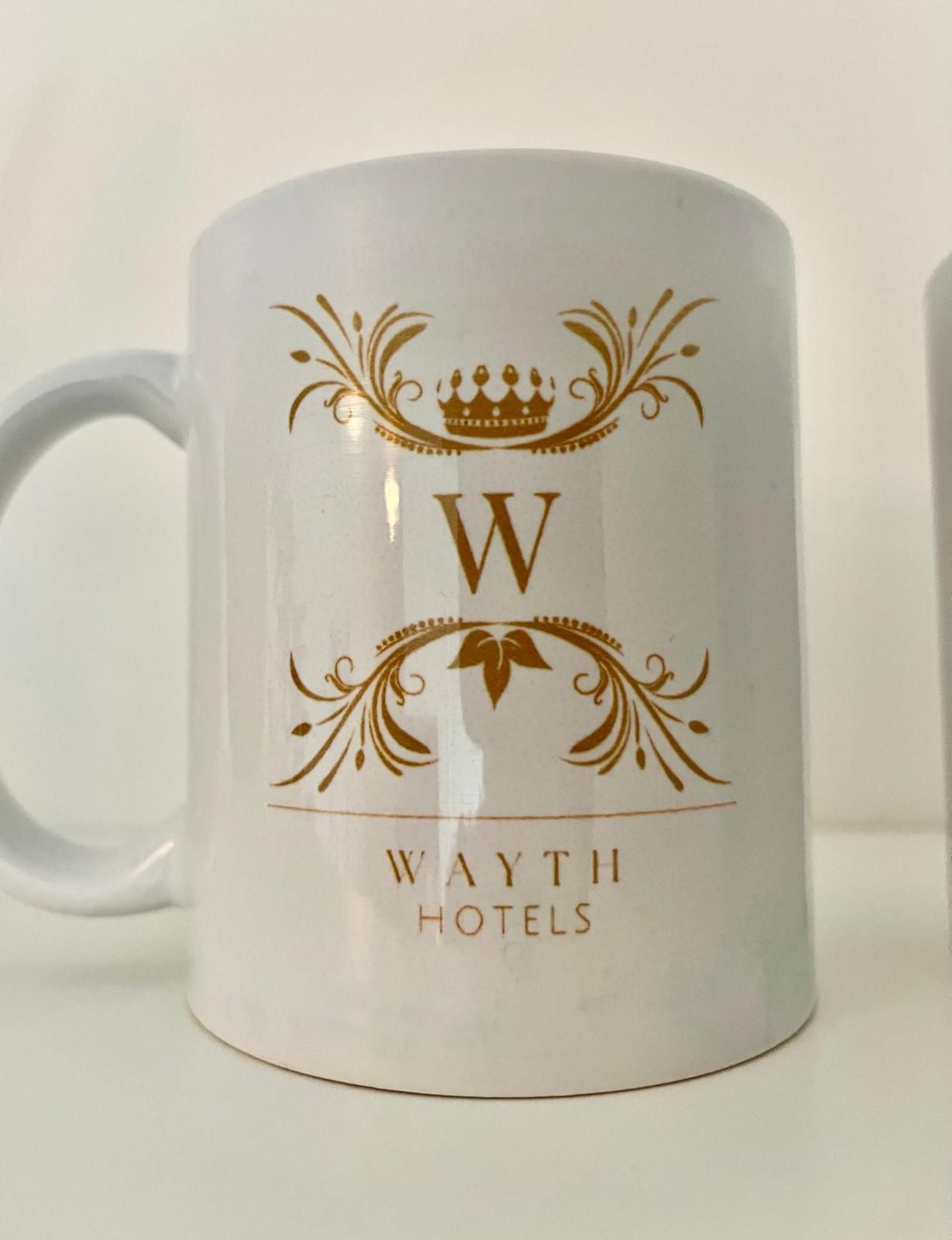 White mug with gold Wayth Hotels logo and decorative crest.